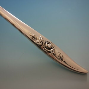 May include: Close-up of a silver fork handle with a rose and leaf design.