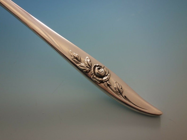 May include: Close-up of a silver fork handle with a rose and leaf design.