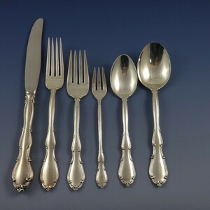 May include: A set of six silver-plated flatware pieces, including a knife, fork, and spoon. The pieces have ornate handles with a floral design.