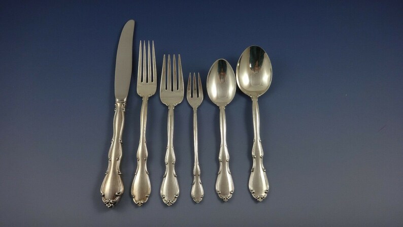 May include: A set of six silver-plated flatware pieces, including a knife, fork, and spoon. The pieces have ornate handles with a floral design.