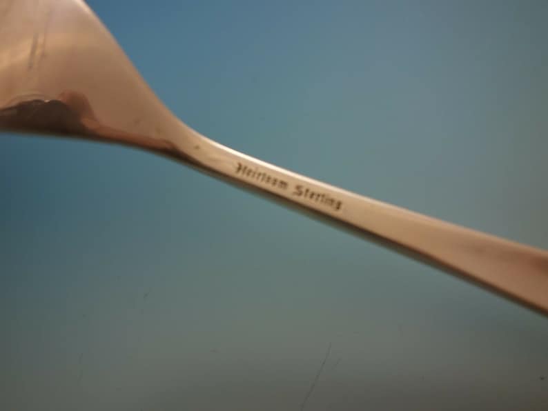May include: Close-up of the back of a silver spoon with the inscription "Heirloom Sterling" on the handle.