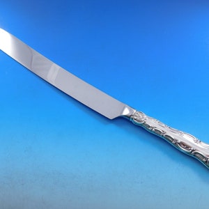 May include: A silver butter knife with an ornate handle. The blade is long and thin, and the handle is decorated with a floral pattern.