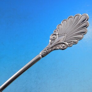 May include: A silver serving spoon with an ornate, fan-shaped design at the end of the handle.