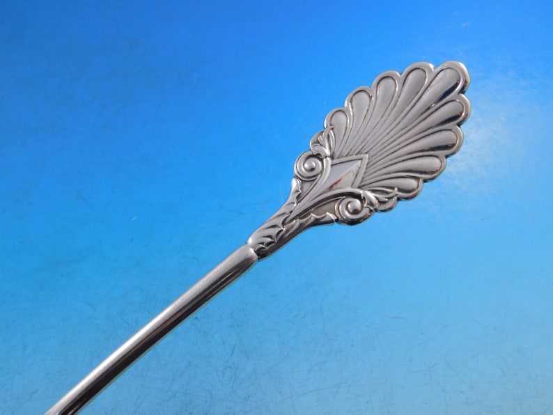 May include: A silver serving spoon with an ornate, fan-shaped design at the end of the handle.