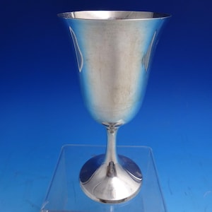 May include: A silver goblet with a flared rim and a slender stem. The goblet has a rounded base and a polished, reflective surface. The background is a gradient of blue.