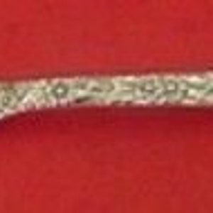 May include: Silver-colored serving fork with a floral pattern on the handle. The two tines have a twisted design. The fork is set against a red background. A decorative utensil for serving.