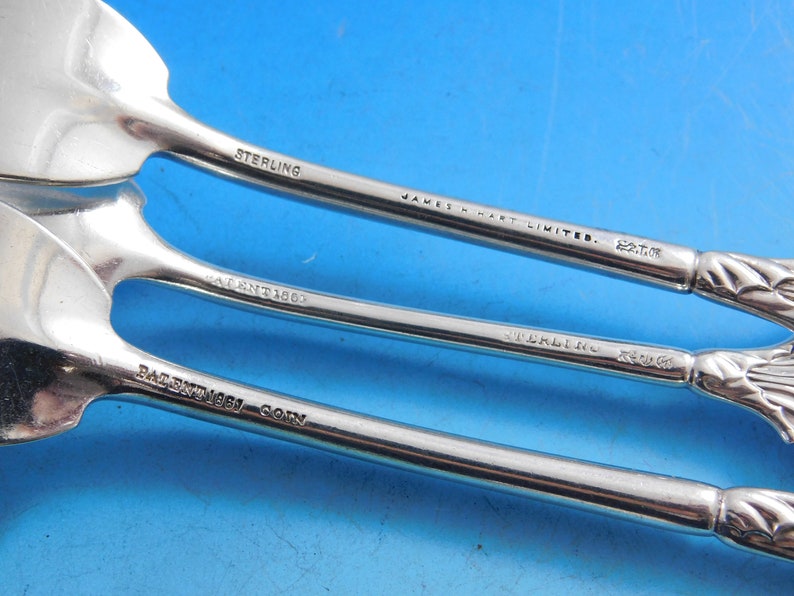 May include: Close-up of the back of three silver spoons with the inscription "STERLING" and "JAMES M. HART LIMITED." The spoons also have the inscription "PATENT 1867" and "PATENT 1862".