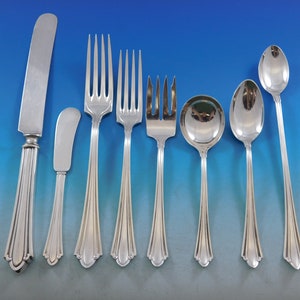 May include: A collection of polished silver flatware, including a knife, butter knife, forks, spoons, and a serving spoon. The silverware has a decorative, ridged handle design and is arranged on a gradient blue background.