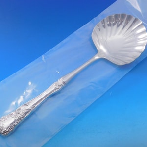 May include: A silver serving spoon with a shell-shaped bowl. The spoon has an ornate handle with a floral design.