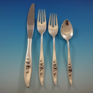 May include: A set of four silver-plated flatware pieces with rose designs on the handles. The set includes a knife, two forks, and a spoon.