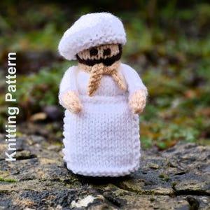 May include: A handmade knitted chef doll wearing a white chef's hat, uniform, and a tan scarf. The doll has a brown beard and tan hands. The words "Knitting Pattern" are printed vertically on the left side of the image.