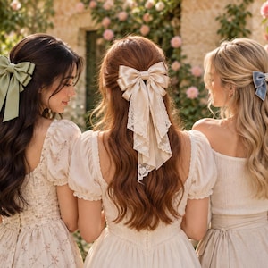 May include: Three hair bows worn in long hair. The left bow is sage green satin. The center bow is champagne satin with lace trim. The right bow is dusty blue velvet with a pearl accent. Each bow is secured in a half-up hairstyle.