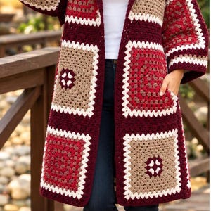 Könnte beinhalten: Eine langärmelige, knielange Strickjacke aus gehäkelten Granny Squares in den Farben Dunkelrot, Beige und Weiß. Das Kleidungsstück verfügt über eine Kapuze, eine offene Vorderseite und zwei Taschen, getragen über einem weißen T-Shirt und einer Jeans.