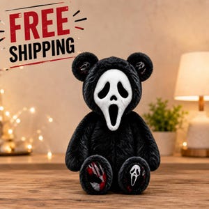 May include: A plush teddy bear with black fur, featuring a white Ghostface mask covering its face. The bear has small Ghostface mask patterns inside its ears and on the soles of its feet, with red accents on the foot pads and ear details.