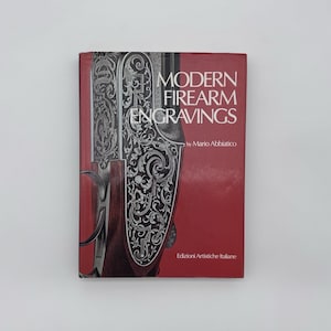 Può includere: Un libro con copertina rigida intitolato Modern Firearm Engravings di Mario Abbiatico, pubblicato da Edizioni Artistiche Italiane. La copertina rossa presenta un'illustrazione dettagliata in bianco e nero di una piastra di arma da fuoco incisa.