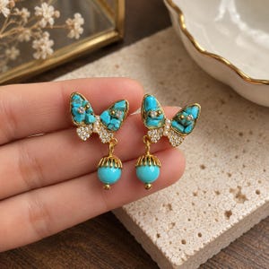 Pendientes colgantes de mariposa turquesa, pendientes de cobre tono dorado con perlas de imitación y circonitas cúbicas.