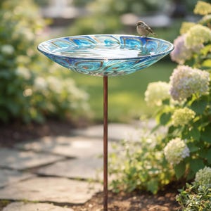 Puede incluir: Un baño para pájaros con un cuenco de cristal circular y poco profundo, decorado con un patrón de remolinos en azul, turquesa y dorado. El cuenco se apoya en un soporte metálico fino de color cobre con una base de tres puntas.