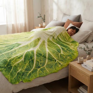 May include: A soft throw blanket featuring a realistic, high-resolution print of a large green cabbage leaf. The blanket displays intricate white veins spreading across vibrant green foliage, covering the bed and providing a textured appearance.