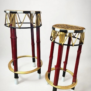 May include: Two tall stools featuring red bamboo-style legs with black and white accents. The circular tops are framed by black and white bands with gold supports, and each stool has a gold circular base ring near the bottom.