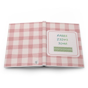 May include: An open hardcover book featuring a light pink and white gingham pattern. The right page displays a white rectangular label with the text "RABBI ZIDNI ILMA" in blue and green, and a green banner with "increase me in knowledge".