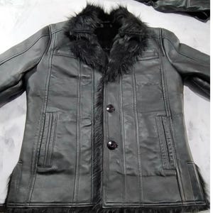 Peut inclure: Une veste noire dotée d'un col en fausse fourrure à poils longs et d'une bordure le long de l'ouverture avant et de l'ourlet. La veste présente une finition lisse, des coutures verticales, deux poches fendues et deux boutons ronds.