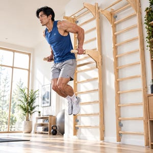 May include: A light-colored wooden wall-mounted stall bar unit featuring horizontal rungs and a detachable dip station attachment. The structure is made of natural wood and is securely fastened to the wall, providing a vertical ladder design.