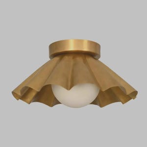 May include: A flush mount ceiling light fixture featuring a wide, scalloped brass shade with a metallic finish. A single, spherical white glass globe bulb is centered within the shade, extending slightly below the bottom edge of the brass metal.