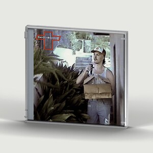 Peut inclure: Un boîtier CD en plastique transparent présentant une image de couverture imprimée d'une personne portant un débardeur blanc, un pantalon clair et une casquette, tenant une boîte en carton et une canette sombre. Le texte American Sweetheart est dans une croix rouge.