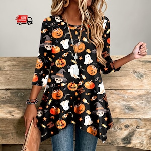 May include: A black long-sleeve tunic top featuring an all-over Halloween print with orange pumpkins, white ghosts, skulls wearing witch hats, and the text Trick or Treat. The garment has a round neckline and a pointed hemline at the bottom.