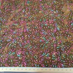 以下が含まれることがあります： ピンク、ブルー、グリーンのフローラルデザインが繰り返しパターン化されたブラウンの生地。生地はバティックスタイルです。