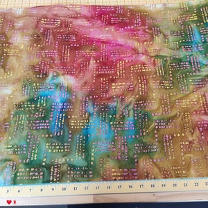 以下が含まれることがあります： 正方形と点の幾何学模様が施されたカラフルな生地。生地は茶色、ピンク、緑、青のブレンドです。