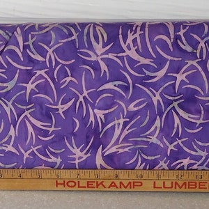 Könnte beinhalten: Lilafarbener Stoff mit einem weißen und hellrosa Batik-Muster aus abstrakten Formen. Der Stoff wird mit einem Holzlineal gemessen, auf dem "HOLEKAMP LUMBER CO." steht.