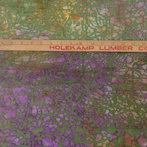 May include: Green fabric with a batik pattern of purple, orange, and brown. The fabric has a mottled, textured look.
