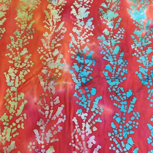 以下が含まれることがあります： 白と青の バティック模様が施された赤い布。布は「RY FURNITURE WORLD」と書かれた黄色の定規で測定されています。布には「mdg - 10」という文字が書かれています。