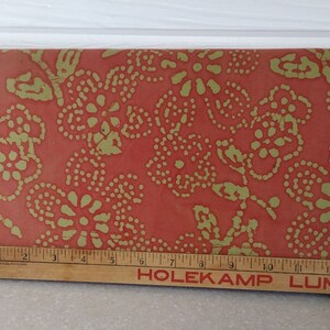 May include: A close-up of a red fabric with a gold floral pattern. The fabric has a textured surface and a repeating pattern of small circles and flowers.
