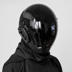 Puede incluir: Un casco integral negro con una visera oscura, lisa y reflectante que cubre toda la parte frontal. El casco incluye accesorios laterales mecánicos con tornillos visibles y un panel de malla texturizada cerca del área de la oreja, usado con una capucha negra.