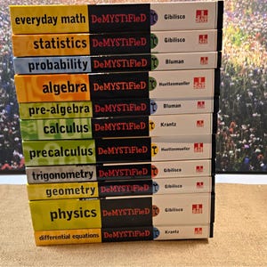 May include: A stack of eleven educational books from the DeMYSTiFieD series, including titles like Everyday Math, Statistics, Probability, Algebra, Pre-Algebra, Calculus, Precalculus, Trigonometry, Geometry, Physics, and Differential Equations.