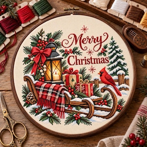 May include: A circular cross-stitch embroidery in a wooden hoop featuring a Christmas scene with a lantern, a red plaid blanket on a wooden sled, wrapped gifts, a red cardinal bird, and the text Merry Christmas in red script lettering.
