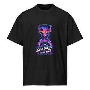 Könnte beinhalten: Ein schwarzes Kurzarm-T-Shirt mit einer Grafik, die eine Sanduhr mit einer Strand-Sonnenuntergang-Szene und einem Gamecontroller zeigt. Der Text lautet LOADING... SINCE 2013 und SOME GAMES ARE WORTH THE WAIT in leuchtenden Neonfarben Blau, Pink und Lila.