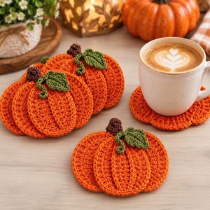May include: A set of orange pumpkin-shaped crochet coasters, each featuring a dark brown stem and a single green leaf. The coasters are crafted with a textured stitch pattern, and one coaster is shown supporting a white ceramic mug of coffee.