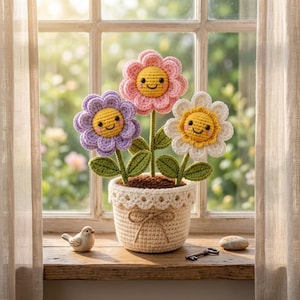 Könnte beinhalten: Drei gehäkelte Blumen mit lächelnden Gesichtern in einem cremefarbenen Häkeltopf. Die Blumen sind rosa, lila und weiß mit gelben Mitten und grünen Blättern. Ein kleiner Keramikvogel, ein Metallschlüssel und ein glatter Stein liegen daneben.