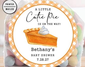 Op de afbeelding: Een witte en oranje cadeauzak met een ronde sticker waarop staat "A Little Cutie Pie Is On The Way!" met een afbeelding van een pompoentaart. De sticker zegt ook "Bethany's Baby Shower 7.28.27".