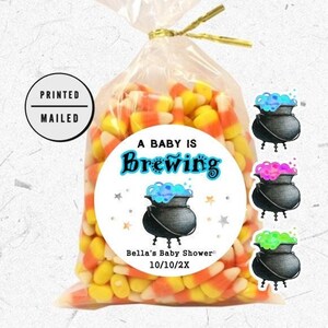 May include: A baby shower favor bag filled with candy corn and a round sticker that says "A Baby is Brewing" with a black cauldron and blue, green, and pink bubbles. The sticker also says "Bella's Baby Shower 10/10/2X".