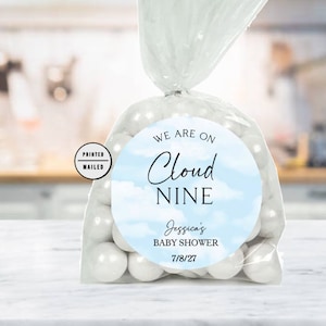 May include: A round blue and white baby shower favor tag with the text "We are on Cloud Nine" and "Jessica's Baby Shower 7/8/27".