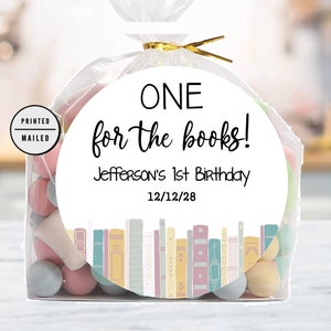 K&ouml;nnte beinhalten: Ein wei&szlig;er runder Aufkleber mit dem Text "ONE for the books!" und "Jefferson's 1st Birthday 12/12/28". Der Aufkleber zeigt eine bunte Illustration eines B&uuml;cherregals mit B&uuml;chern.