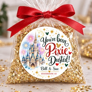 May include: A clear plastic bag filled with gold glitter, tied with a red satin ribbon. A circular label features a castle, fireworks, and the text "You've been Pixie Dusted! Bill & Sue STATEROOM: 65" with small mouse-ear icons.