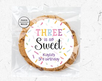 May include: A white round sticker with colorful sprinkles and the text "THREE is so Sweet Kayla's 3rd birthday".
