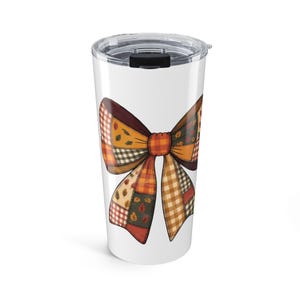 May include: A white stainless steel tumbler with a clear plastic lid featuring a large, central graphic of a bow. The bow is composed of various patchwork patterns in autumn colors including orange, brown, and cream, with leaf motifs and checks.
