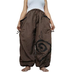 Puede incluir: Pantalones marrones de corte holgado con un patrón de rayas verticales y un gran gráfico de espiral negro en la pierna izquierda. Estos pantalones incluyen una cintura elástica con cordón, bolsillos laterales con borde negro y puños ajustados.