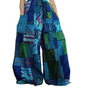 Puede incluir: Pantalones de pierna ancha con un diseño de patchwork en varios tonos de azul y verde. La prenda incluye una cintura con cordón, dos bolsillos laterales grandes y paneles con patrones de teñido anudado y símbolos impresos en la tela.